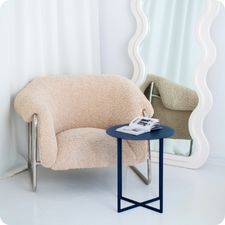 Granatowy stolik metalowy LOOM SIDE CHROMA FØRM ustawiony przy fotelu.